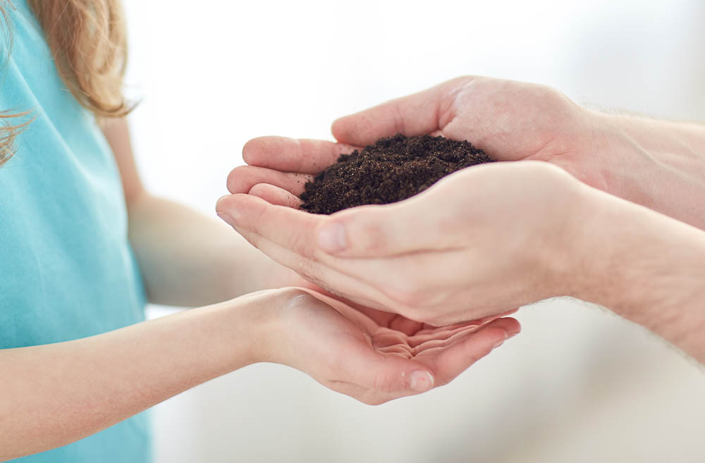 people, charity, family and legacy concept - close up of father and girl holding soil in cupped hands at home
